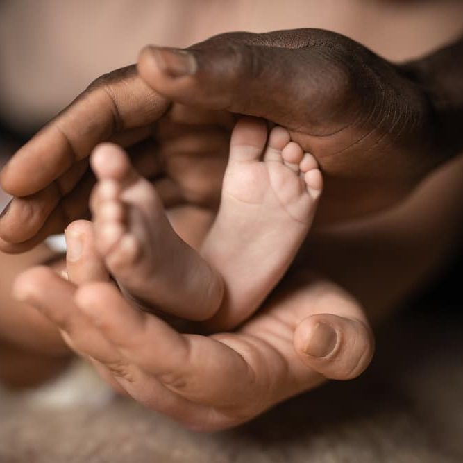 Interracial Family Holding Baby Feet In Hands.